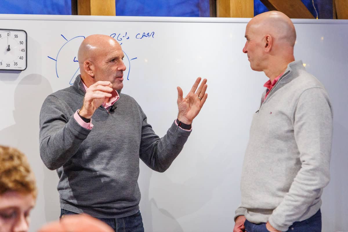 Executive team coaching at the whiteboard: a coach gestures through strategy with another leader during a Monkhouse and Company workshop.