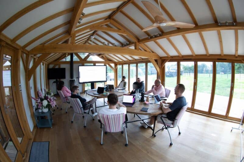 Modern meeting room with large windows, wooden beams, and a group of professionals collaborating.