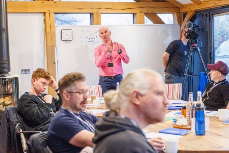 Coach presenting at a whiteboard while a team works on its team charter