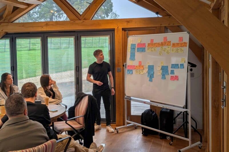Young man presenting ideas on a whiteboard to a group of colleagues.