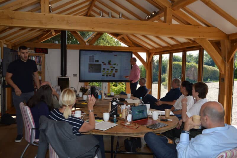 Business meeting in a bright, wooden conference room with a large screen display.