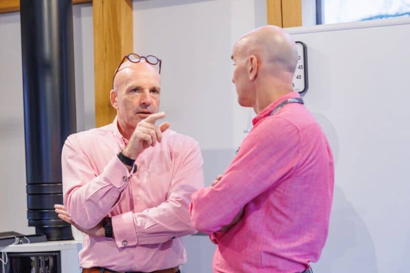 Two men in pink shirts having a serious discussion in an office setting.