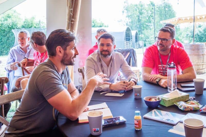 Founders around a workshop table in animated discussion, the kind of peer challenge that replaces a CEO's private one-on-ones with each executive