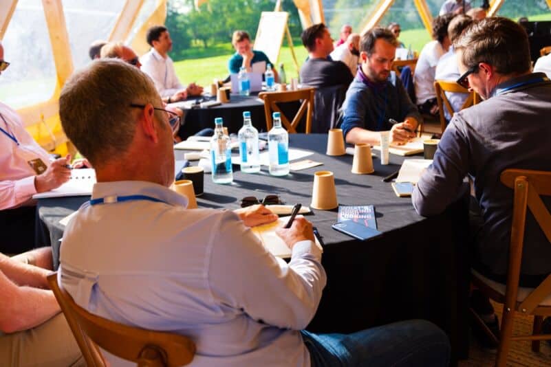 Business professionals attending an outdoor conference under a tent.